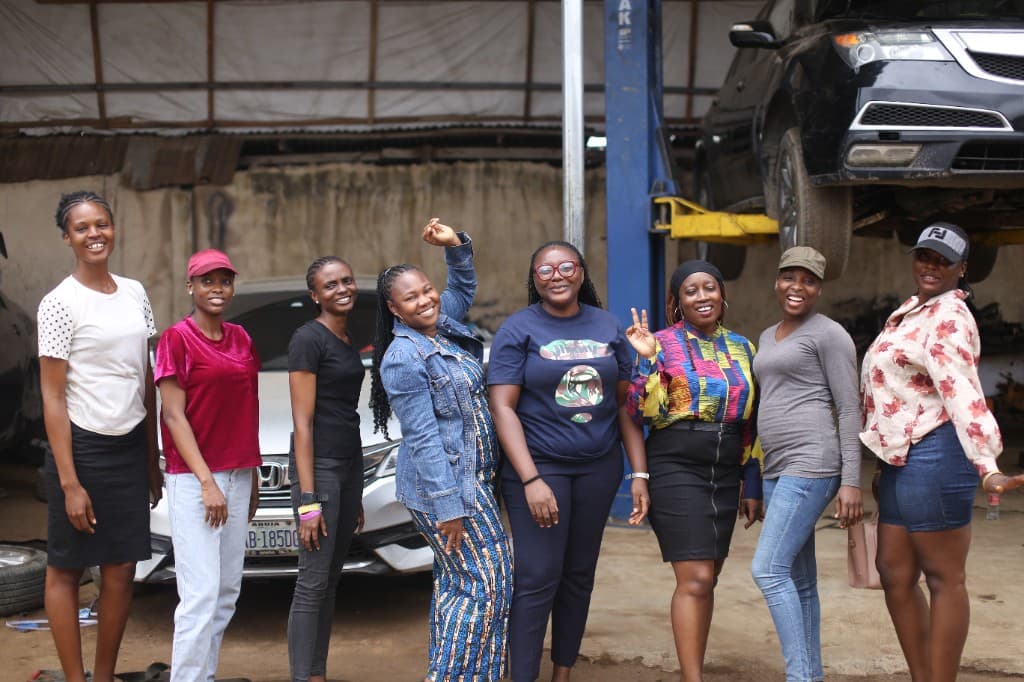 Group of smiling women posing inside an automotive repair workshop